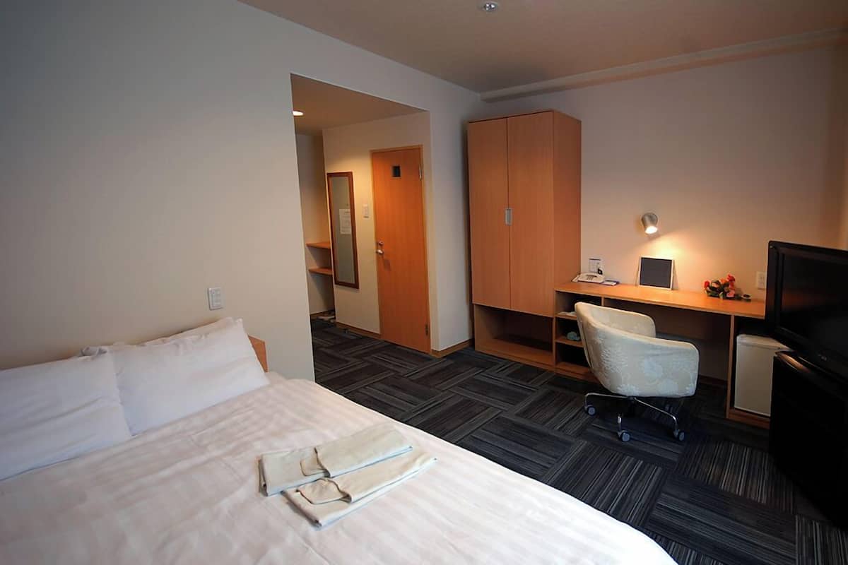 A hotel room with a bed, a desk with a computer, a TV, and a wardrobe.