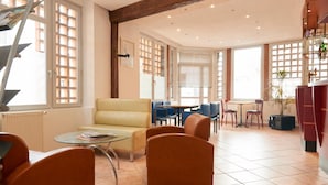 A spacious room with a yellow sofa, orange armchairs, a glass coffee table, and a dining area with blue chairs. - Chambres d'Hôtes du Colvert (Forges-les-Eaux)