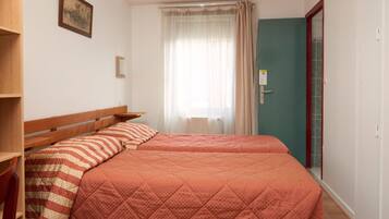 A bedroom with two beds, a wooden headboard, a window with sheer curtains, and a door with a red frame.