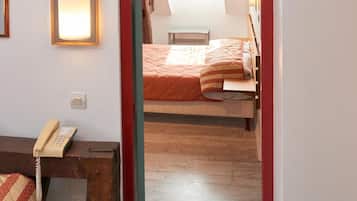 A room with a wooden ceiling, a bed with orange bedding, a telephone on a wooden table, and a green stool.