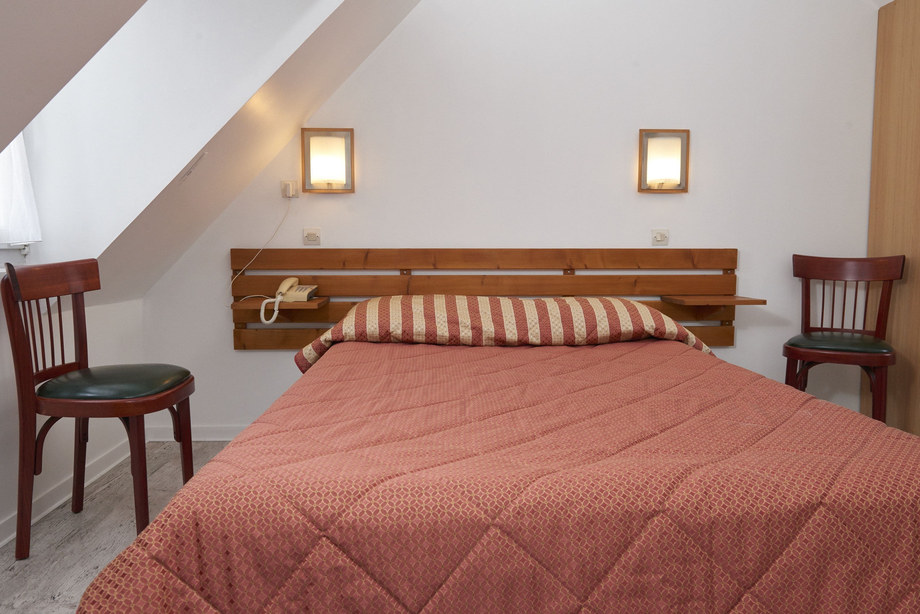 Un dormitorio con una cama, dos sillones, una mesita de noche y dos lámparas de pared.