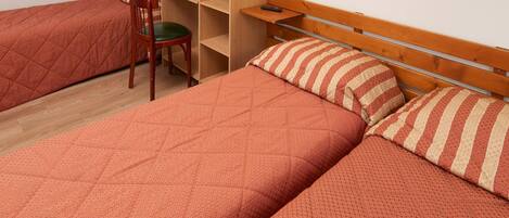 A room with two beds, a chair, a shelf, and a wall-mounted shelf.