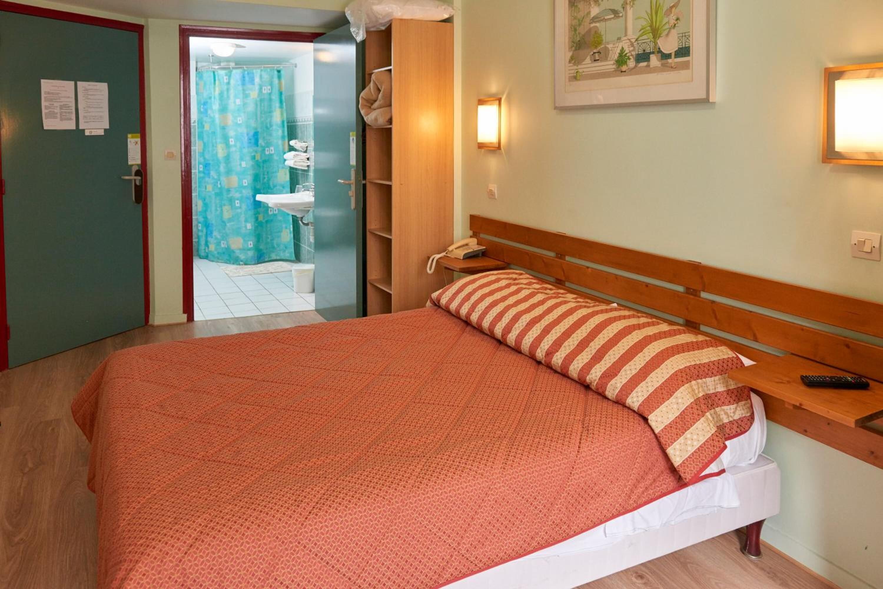 A hotel room with a bed, a wooden nightstand, a telephone, and a bathroom visible through an open door.
