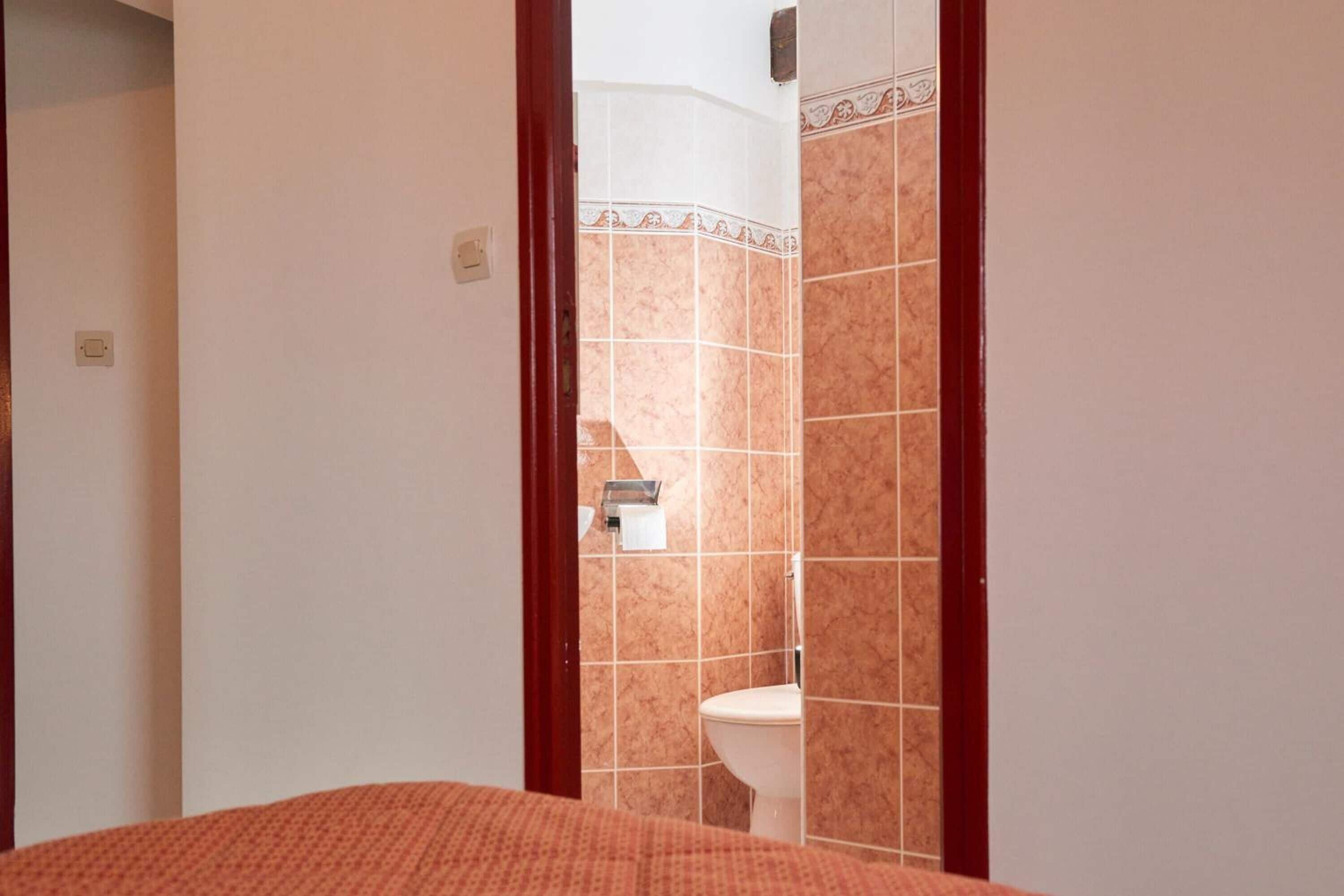 A hotel room with a bed, a bathroom with a toilet and a shower, and a door leading to another room.