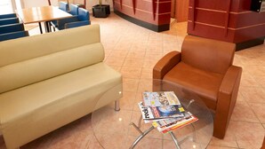 A hotel lobby with a beige sofa, a brown armchair, and a glass table with magazines. - Chambres d'Hôtes du Colvert (Forges-les-Eaux)