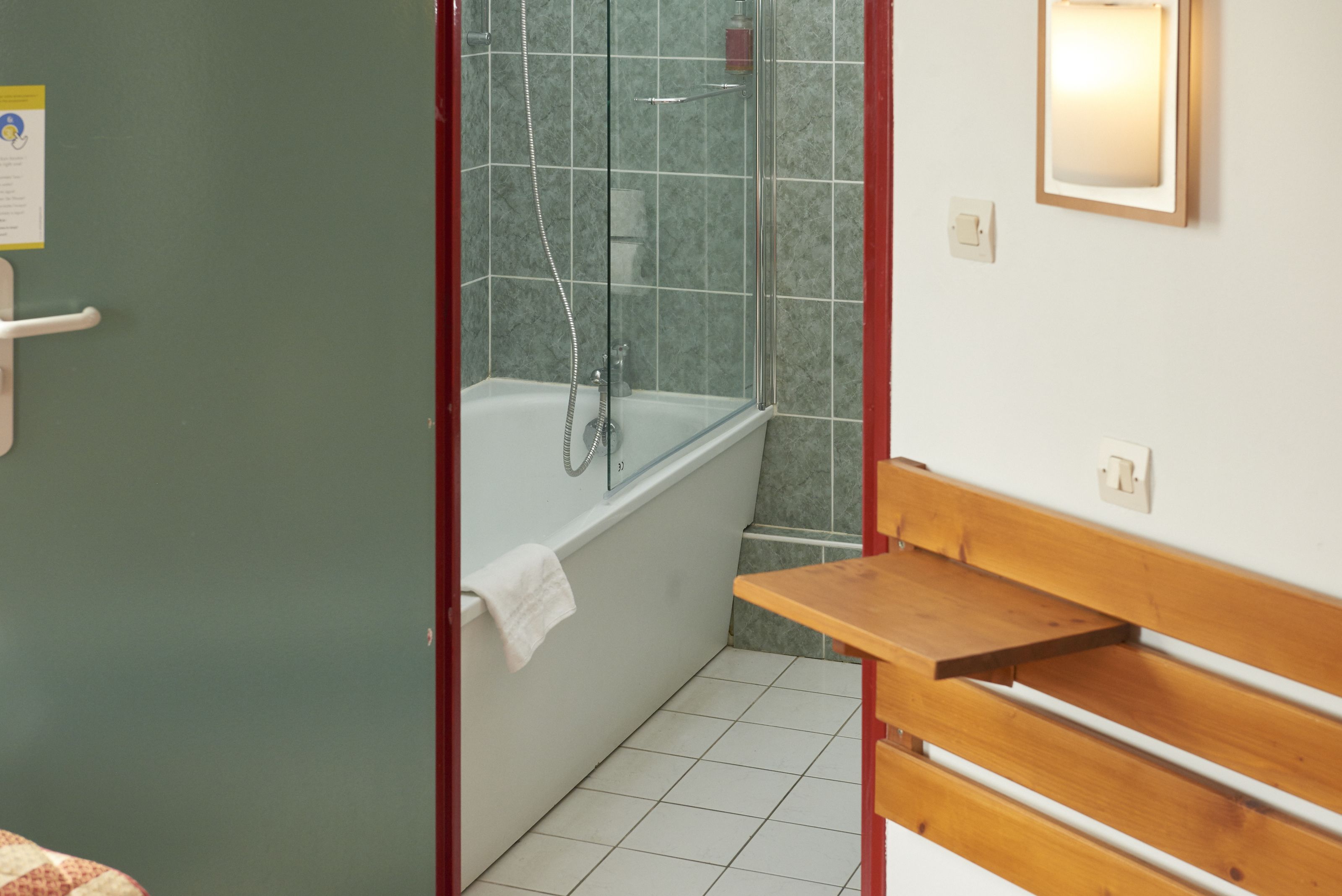 Een badkamer met een badkuip, een douche, een houten bankje en een betegelde vloer.
