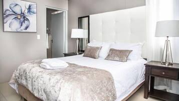 A hotel room with a large bed, a bedside table with a lamp, a mirror, and a painting of a flower on the wall.