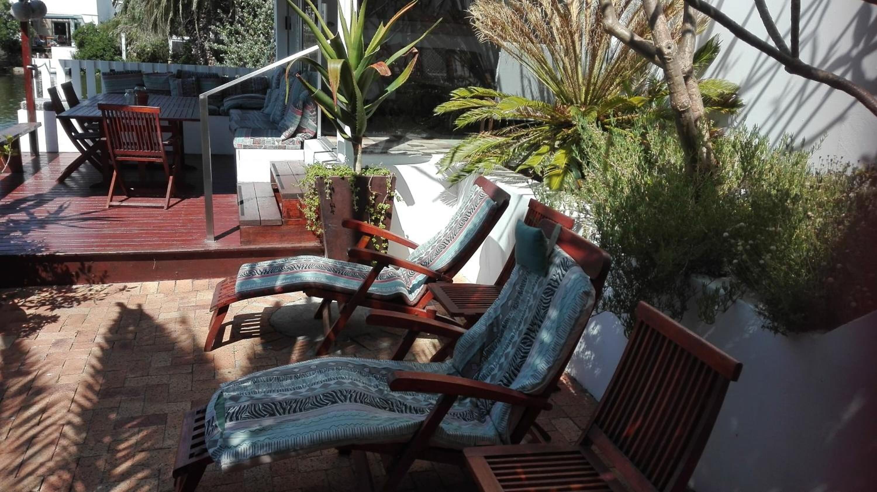 A patio area with two wooden lounge chairs, a small table, and a white wall with greenery.