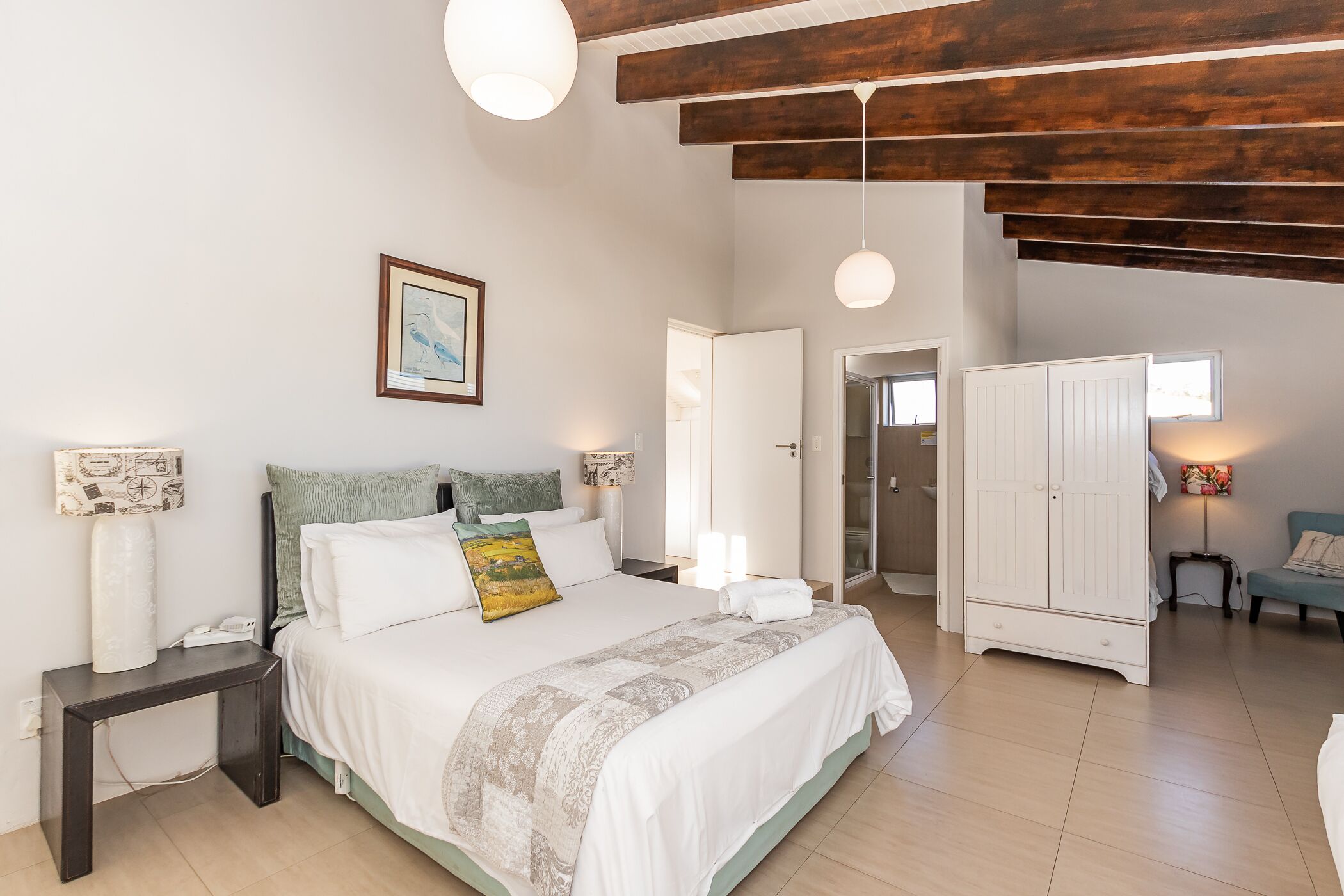 A bedroom with a bed, bedside tables, a wardrobe, and a door leading to another room.