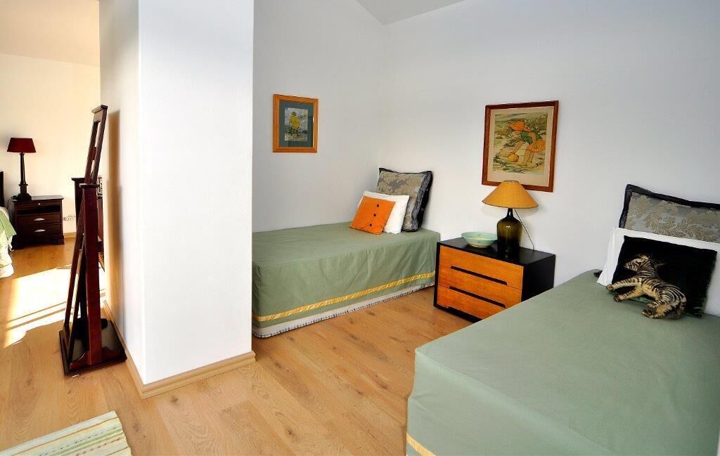 A bedroom with two beds, a nightstand, a lamp, and a guitar against the wall.