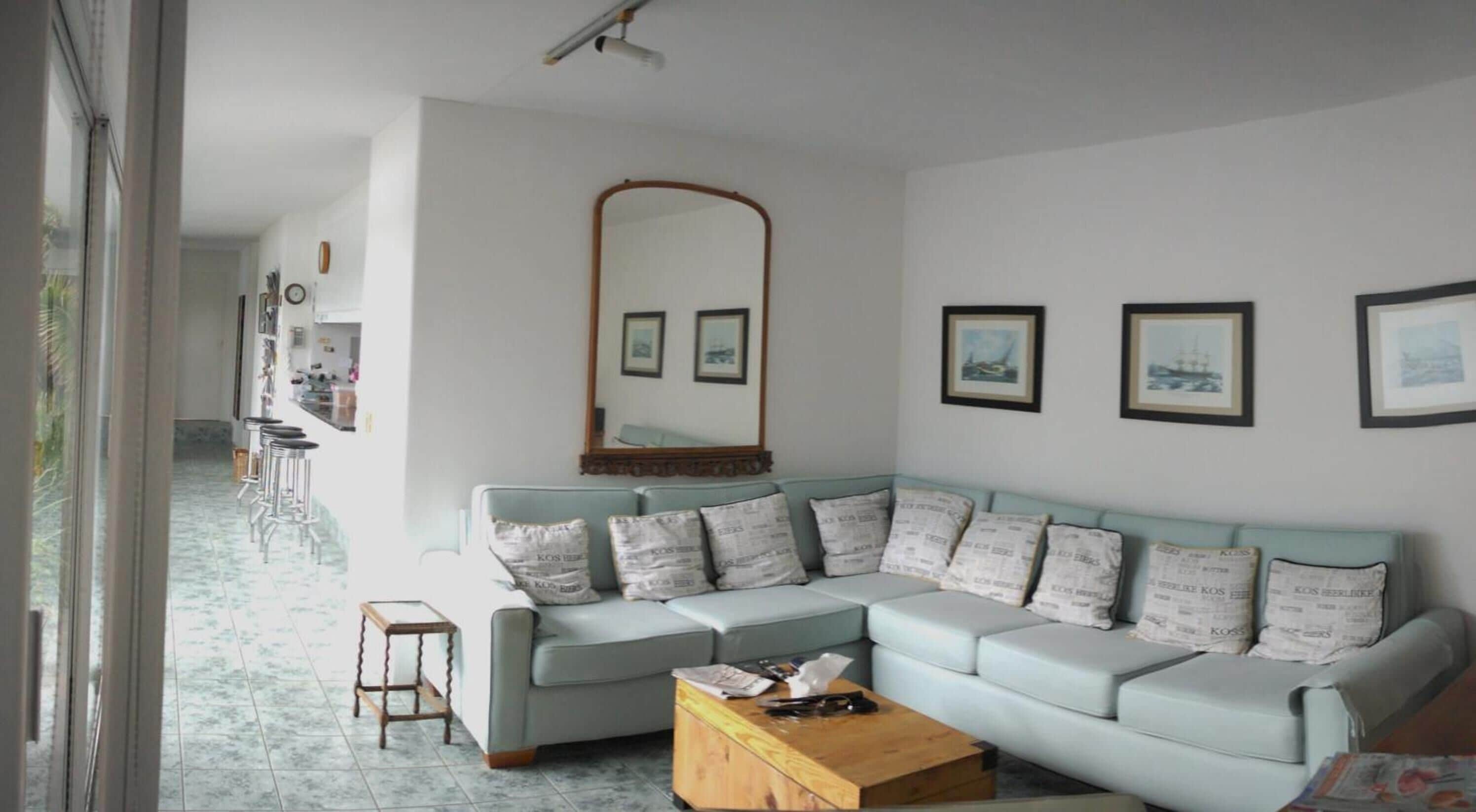 Ein Wohnzimmer mit einem hellblauen Modulsessel, einem Holztisch und einem großen Spiegel über dem Sofa.