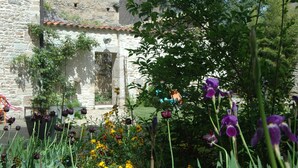 A garden with various flowers and a stone building in the background. - Le Clos de l'Abbaye (Cluny)