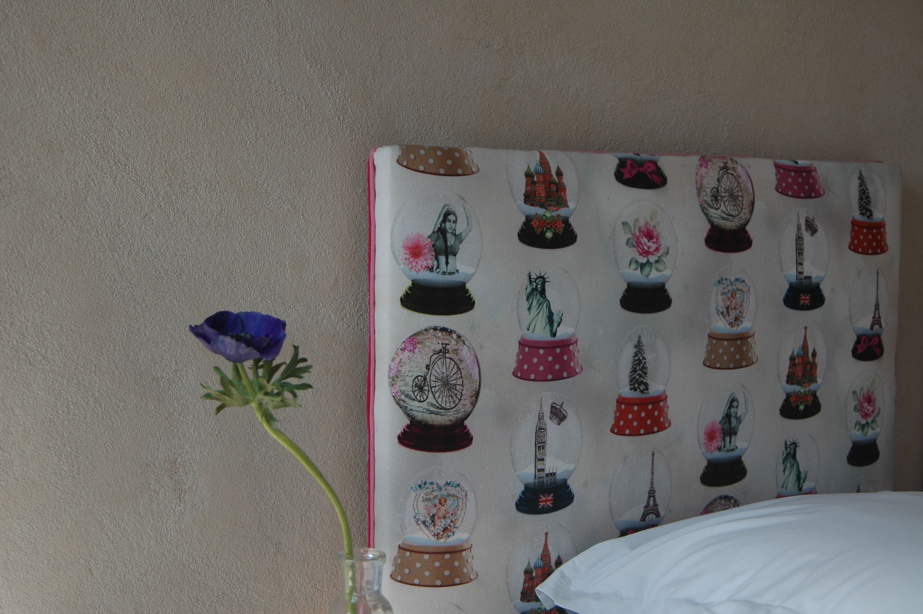 Ein Zimmer mit einem gemusterten Kopfende, einer Vase mit einer einzelnen Blume und einem Bett mit weißer Bettwäsche.