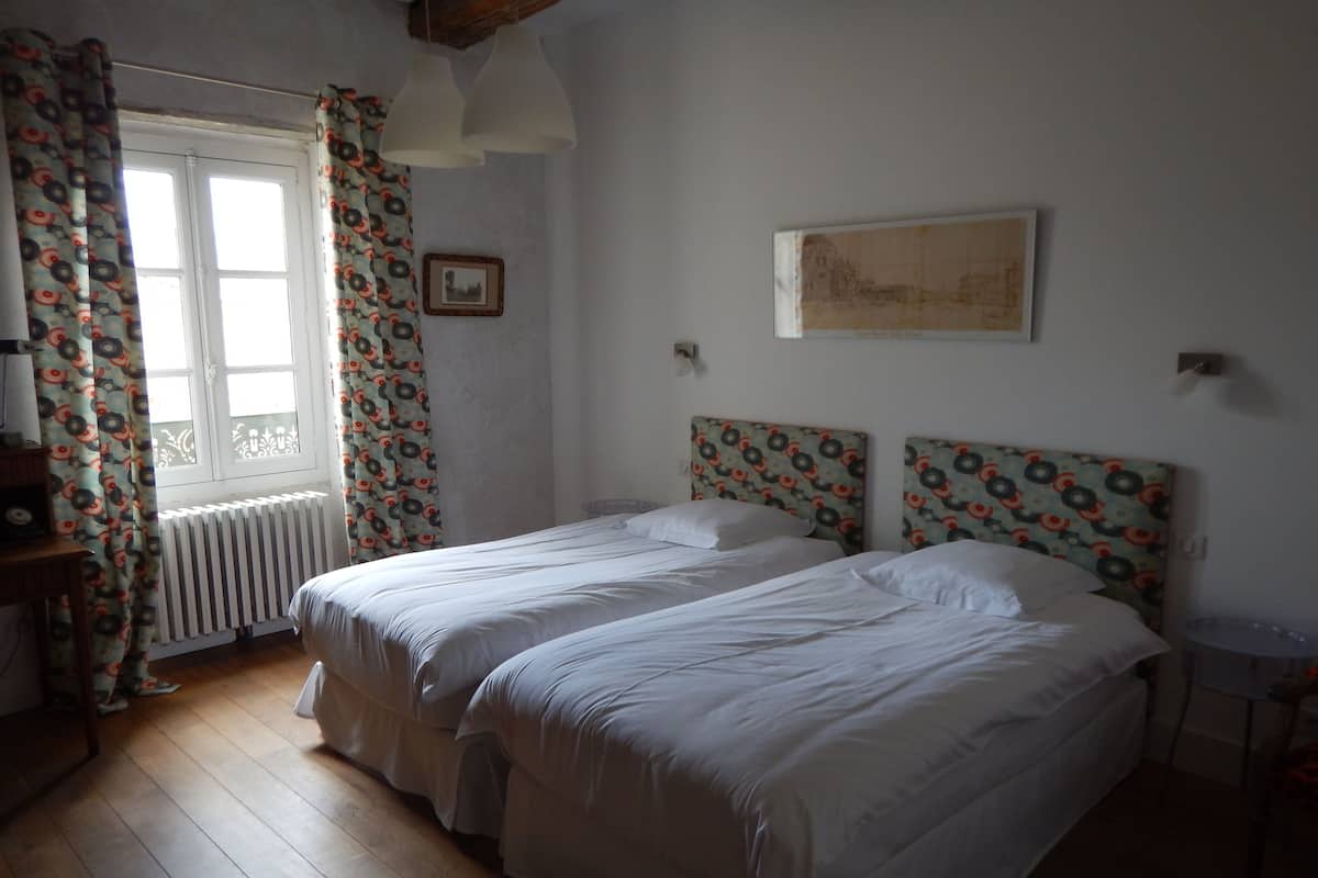 A bedroom with two beds, a radiator, a window with curtains, and a framed picture on the wall.