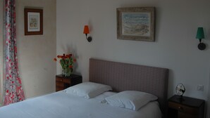 A neatly made bed with white linens, a nightstand with a lamp, a framed picture on the wall, and a vase with flowers on the nightstand. - Le Clos de l'Abbaye (Cluny)