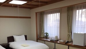 A hotel room with two beds, a dining table, tatami mats, and a view of the outside through large windows. - Shimabara Station Hotel (Shimabara)