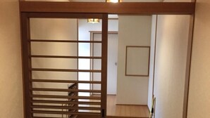 A narrow hallway with a wooden sliding door leading to a room. The floor is tiled, and there is a light fixture on the ceiling. - Shimabara Station Hotel (Shimabara)
