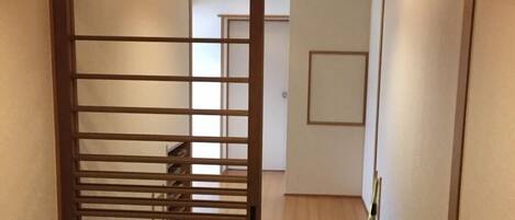 A narrow hallway with a wooden sliding door leading to a room. The floor is tiled, and there is a light fixture on the ceiling.