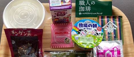 A tray with various packaged food items including a bowl of soup, a packet of instant noodles, a pack of tea, and other snacks.
