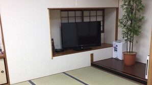 A room with tatami flooring, a low table with chairs, a television on a shelf, and a potted plant. - Shimabara Station Hotel (Shimabara)