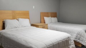 A hotel room with two beds, each with a wooden headboard and white bedding. There is a nightstand between the beds. - Superlodge (New Castle)