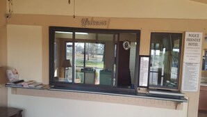 A reception desk with a 'Welcome!' sign, a 'Police Friendly Hotel' sign, and a view of the outside. - Superlodge (New Castle)
