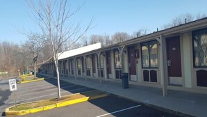 A row of single-story buildings with large windows, a speed limit sign of 10, and a parking lot with marked spaces. - Superlodge (New Castle)
