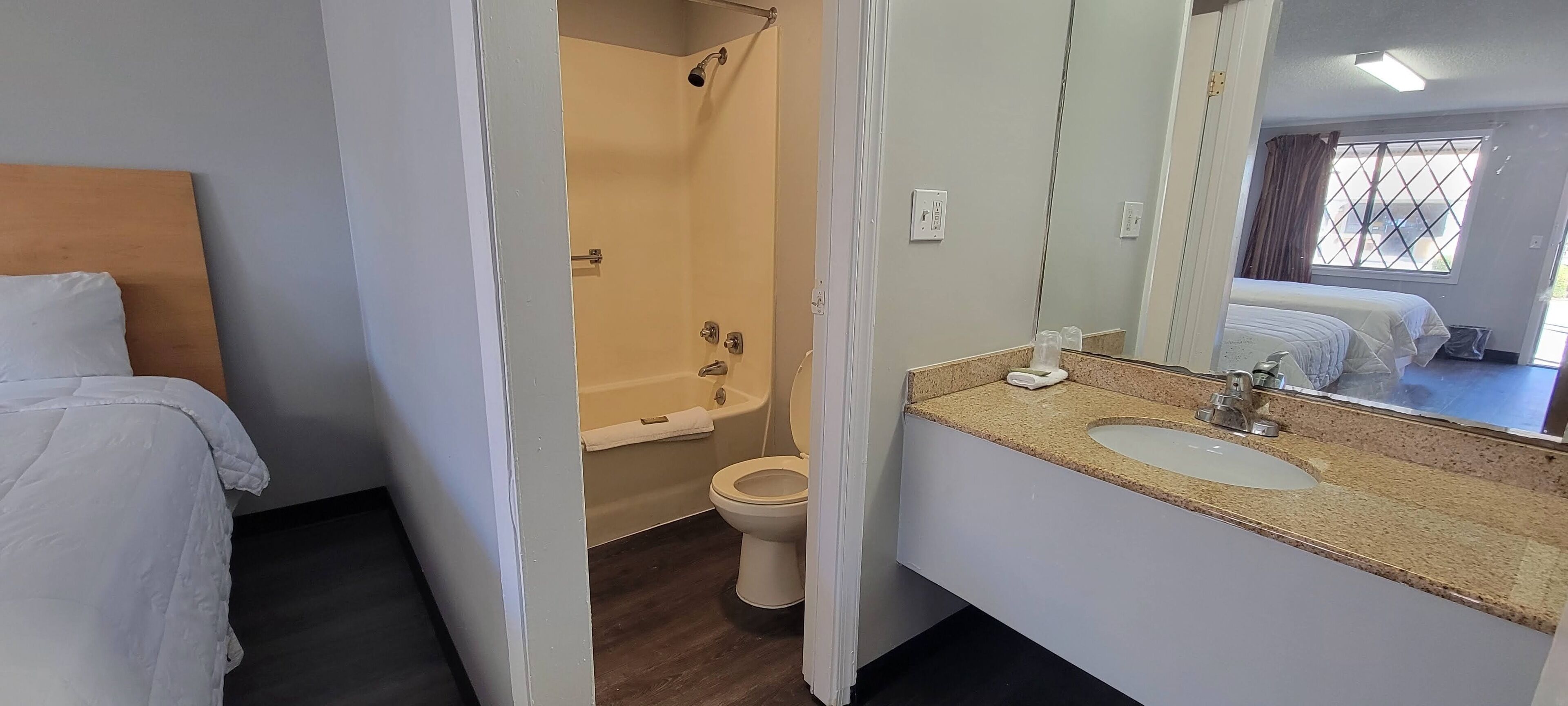 A hotel room with a bed, a shower, a toilet, and a sink with a mirror.