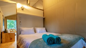 A bedroom with a bed, a wooden bench, and a view of greenery outside.