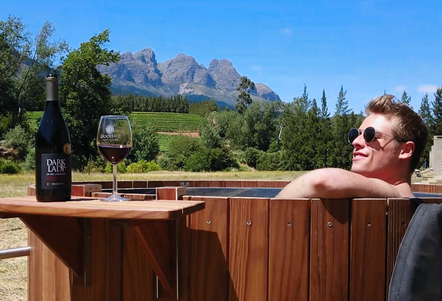 A wooden deck with a bottle of Dark Lady wine and a glass of wine, overlooking a mountainous landscape.
