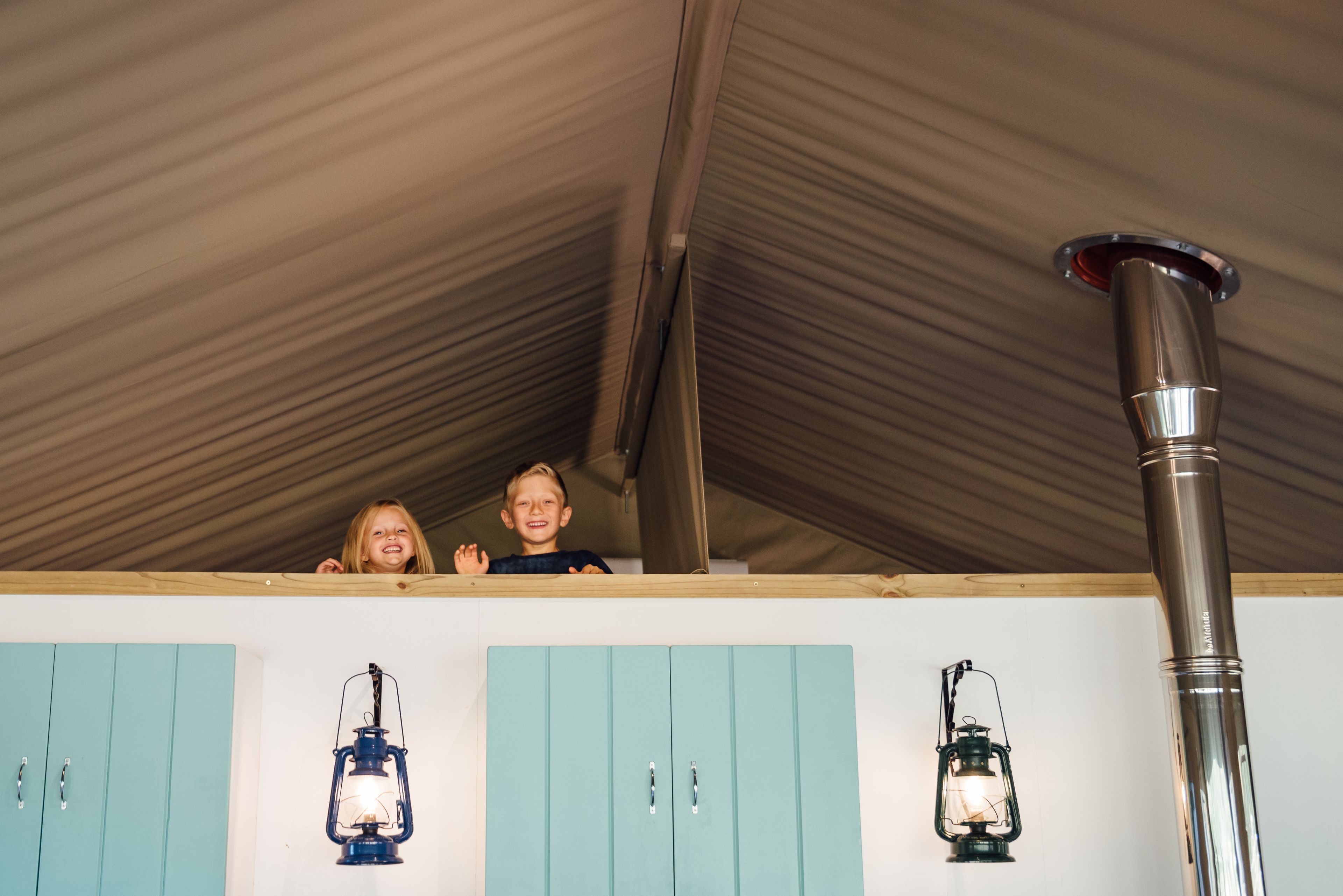 A room with teal cabinets, a metal vent, and two wall-mounted lanterns.