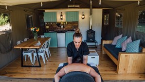 A massage therapy session in a cozy, well-lit room with wooden flooring, a dining area, and a kitchen in the background.