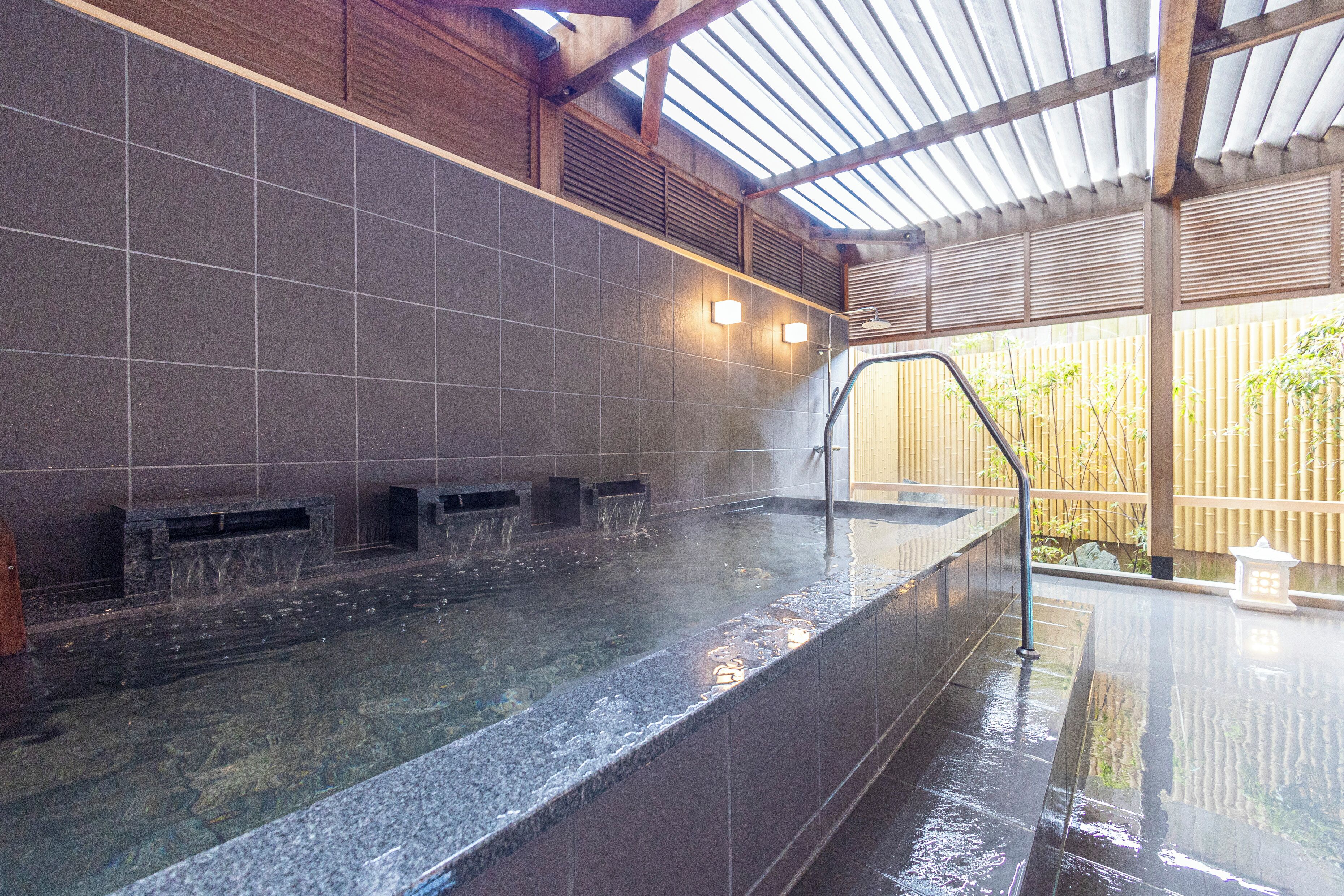 Ein Wellnessbereich mit Whirlpool, gefliesten Wänden und einem Bambuszaun im Hintergrund.