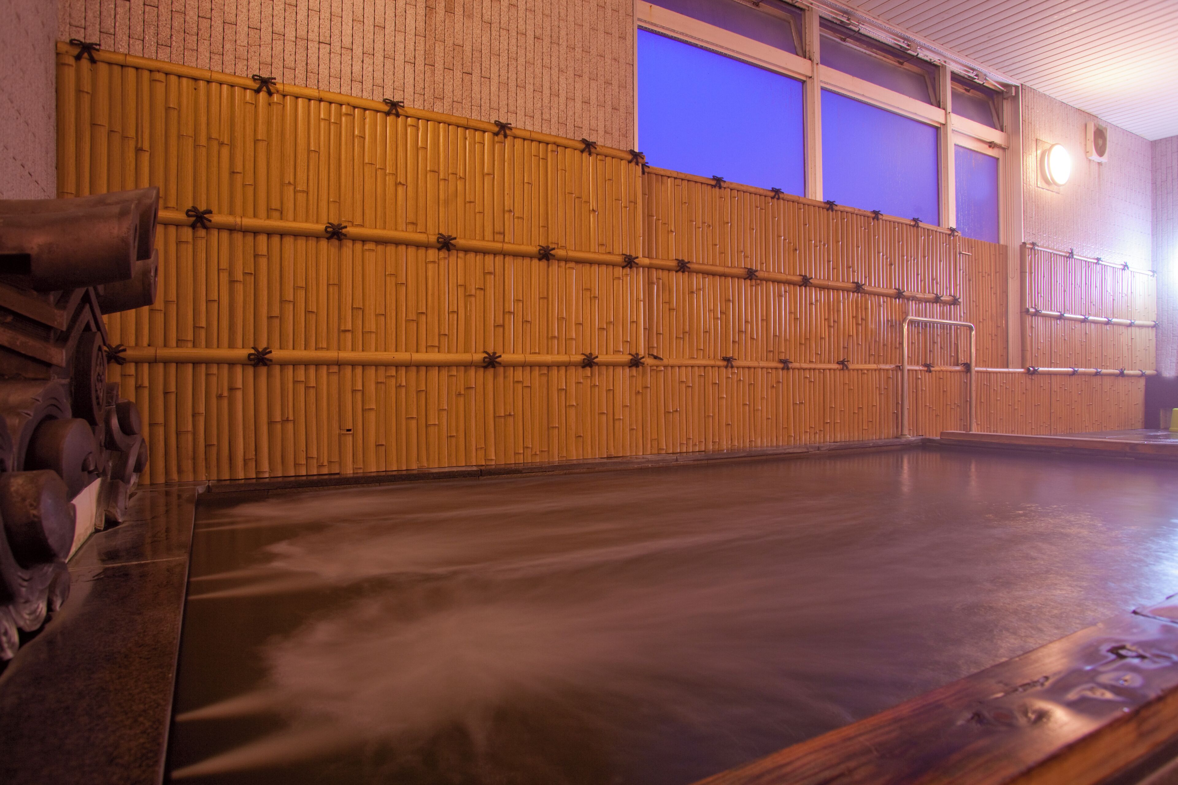 Uma onsen japonesa tradicional com parede de madeira, banho de águas termais e chão de azulejos.