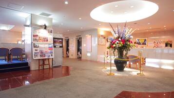 Un vestíbulo de hotel con una recepción, un gran arreglo floral y un tablón de anuncios con varios avisos.