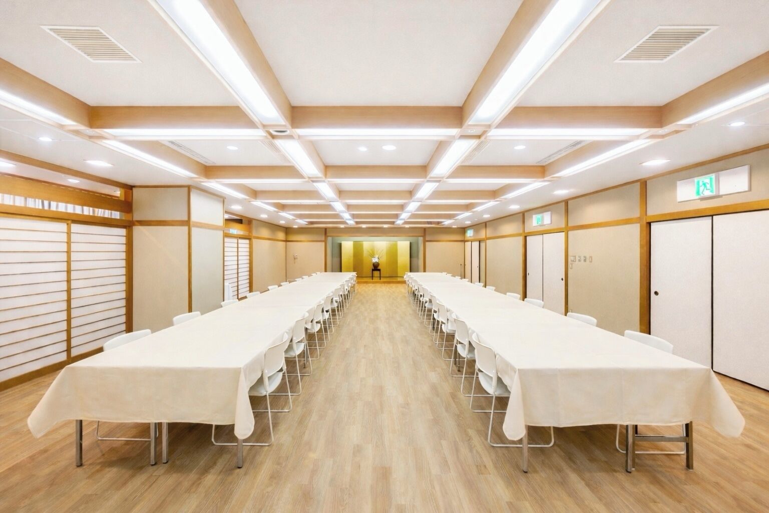 A conference room with long tables, wooden flooring, and recessed ceiling lighting.