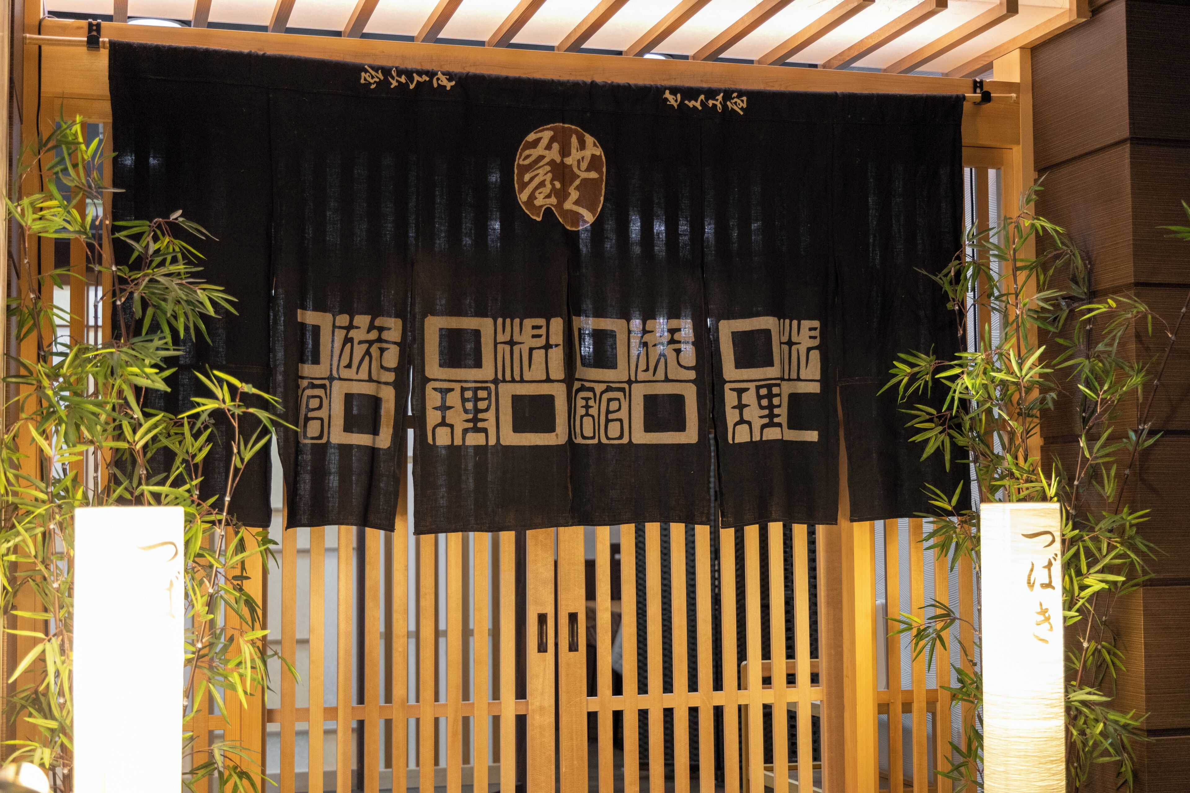 Un torii japonés tradicional con diseño blanco y negro, plantas de bambú a ambos lados y una estructura de madera en la parte superior.