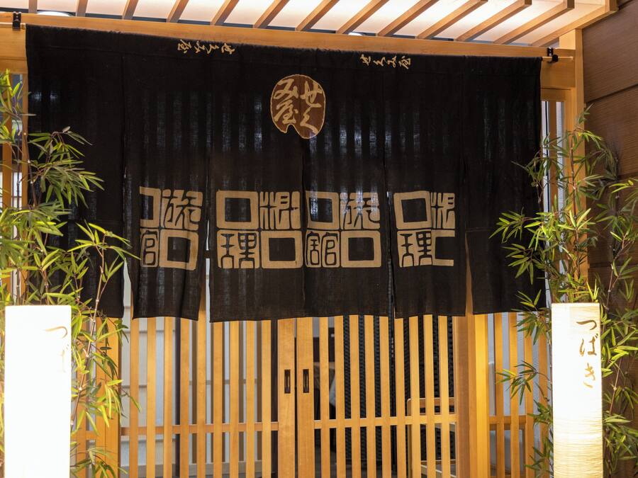 A traditional Japanese gate with a black and white design, bamboo plants on either side, and a wooden structure above.