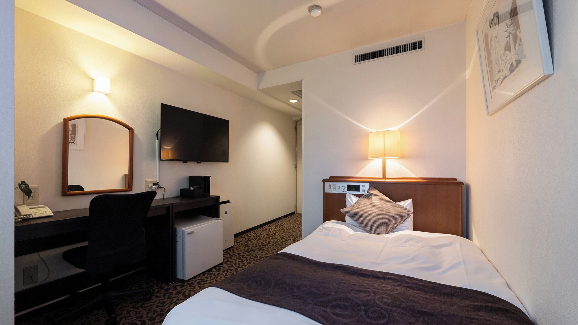 A hotel room with a bed, desk, chair, television, and a small refrigerator.