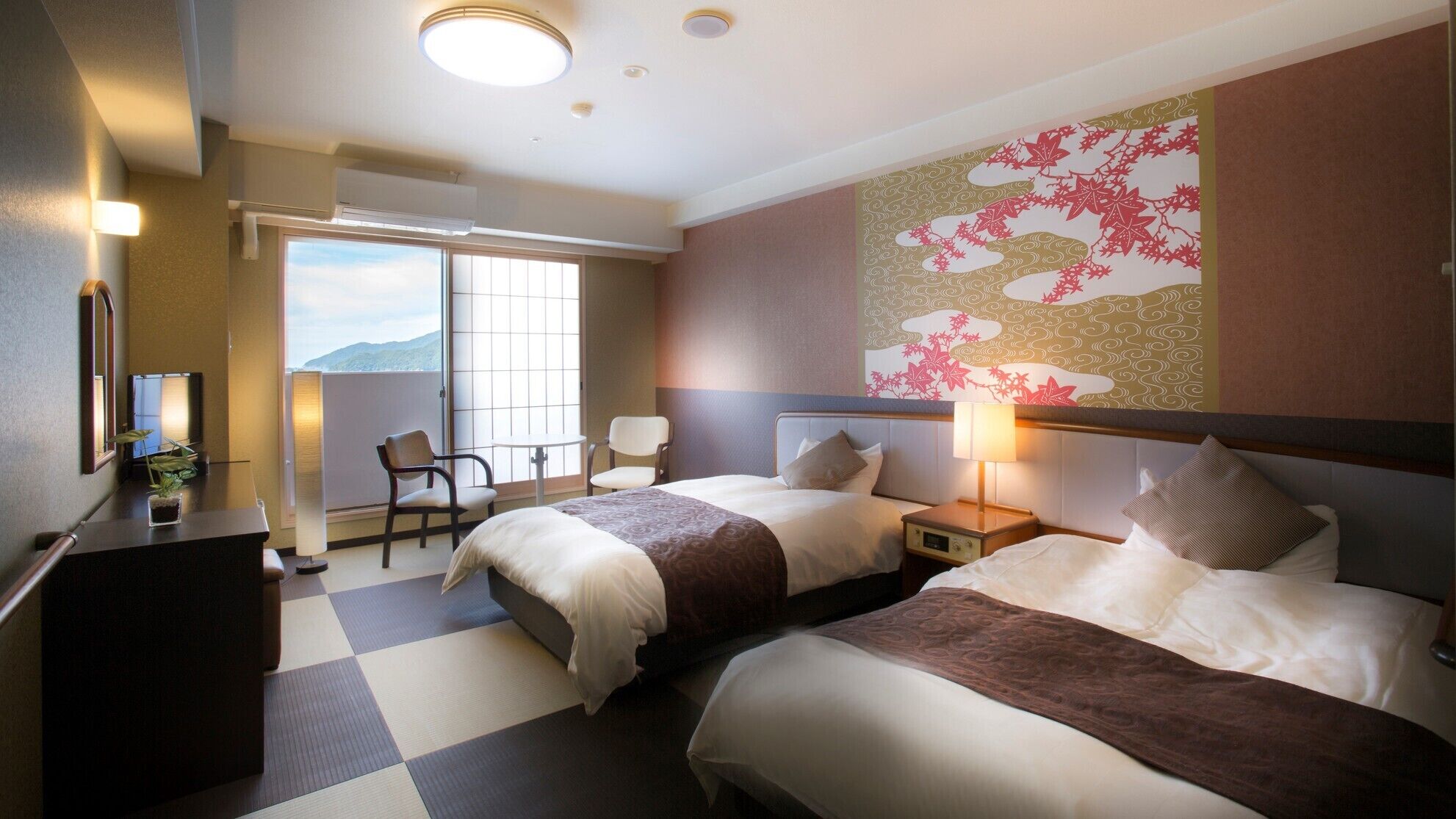 A hotel room with two beds, a desk, a chair, a window with a view, and a decorative wall.