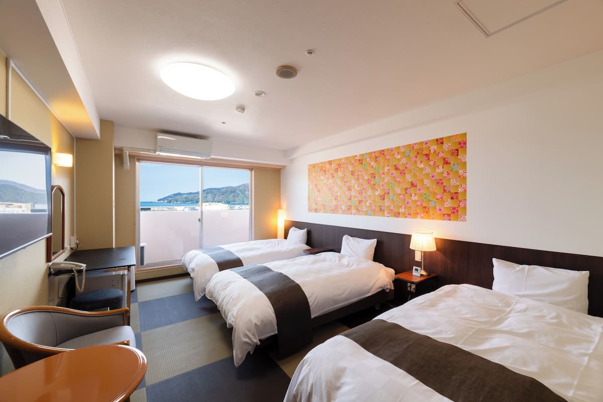 Habitación de hotel con dos camas, un escritorio, una silla, una ventana con vistas y un adorno en la pared.