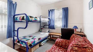 Een slaapkamer met stapelbed, bureau, stoel en een raam met gordijnen.