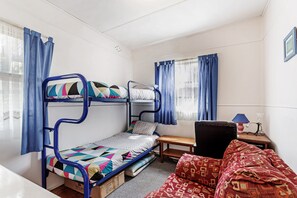 Een slaapkamer met stapelbed, bureau, stoel en een raam met gordijnen.