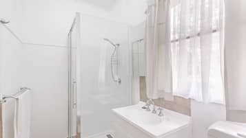 A modern bathroom with a glass-enclosed shower, a white vanity with a mirror, and a toilet.