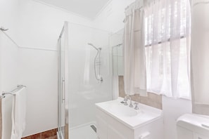 Een moderne badkamer met een douchecabine van glas, een witte wastafel met spiegel en een toilet.