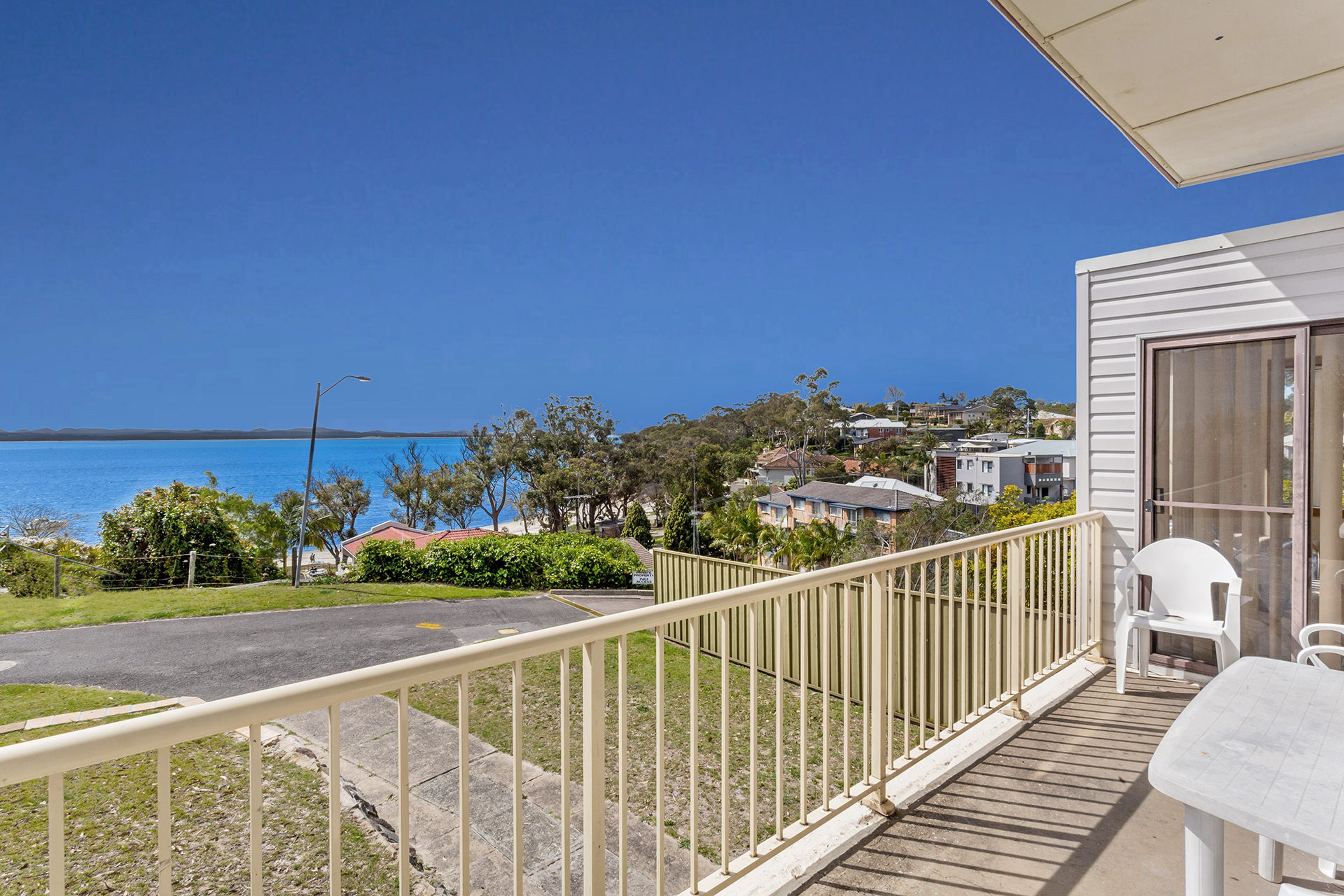 A balcony with a view of the sea, a white chair, and a table.