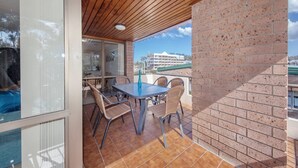 Un balcón con mesa y sillas, un muro de ladrillo y una vista de un edificio al fondo.