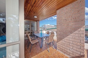 Een balkon met een tafel en stoelen, een bakstenen muur en uitzicht op een gebouw op de achtergrond.