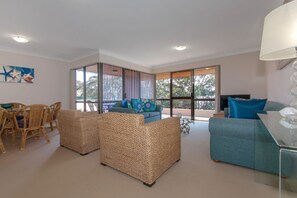 A spacious living area with wicker furniture, a balcony with a view, and a dining area with wicker chairs.