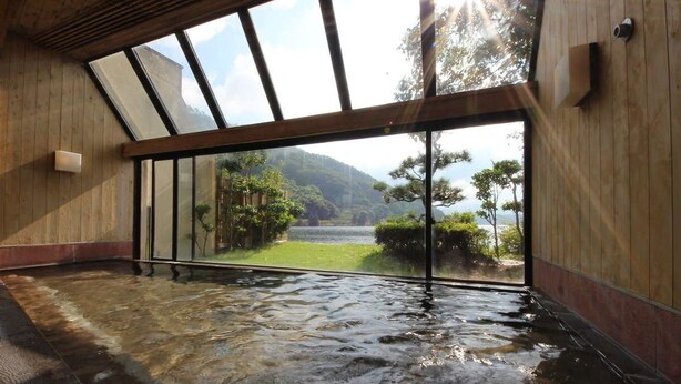 A hot spring bath with a wooden interior and a view of a mountainous landscape through large windows. - Hotel Suigekka (Wakasa)